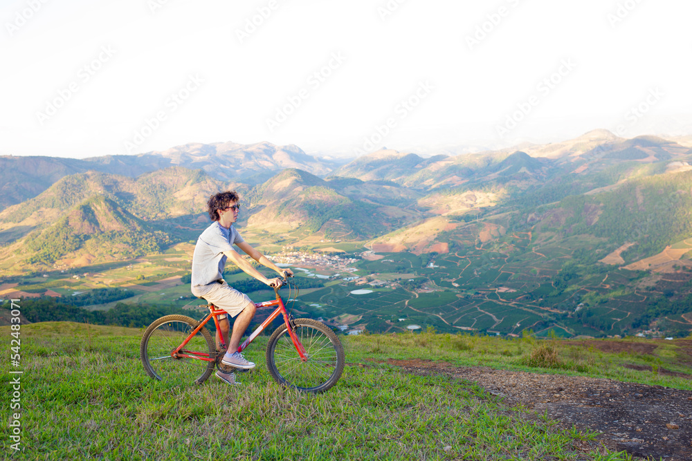 Fototapeta premium Young man riding a bicycle high on a mountain with a valley and mountains in the background.