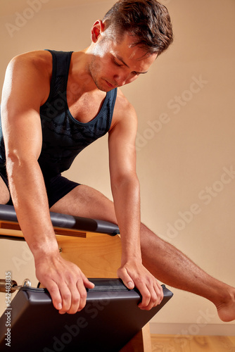 Handsome pilates male instructor performing stretching balance fitness exercise on small barrel equipment, at the pilates studio modern onterior indoor.