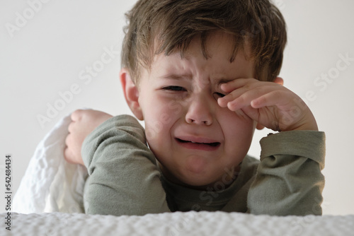 Cute young  boy crying near the bed