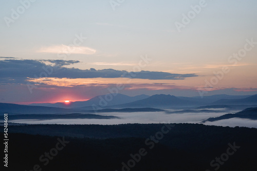 Fototapeta Naklejka Na Ścianę i Meble -  The beginning of a new day dawn in the mountains the sun rises on the horizon, the morning fog, smoke filled the river valley.