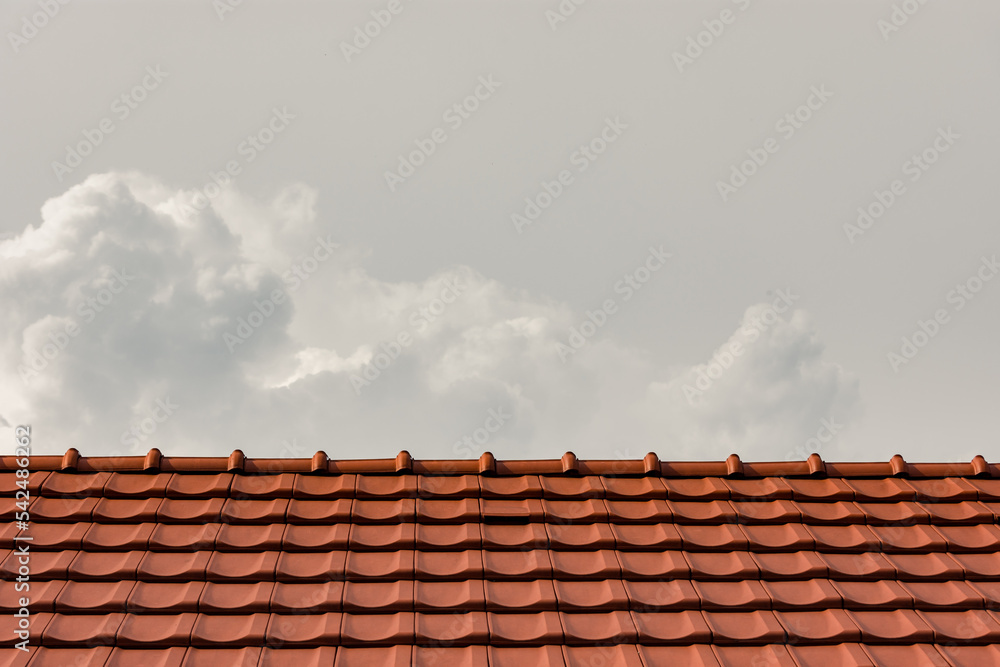 New red tiles on a roof over grey cloudy sky. Real estate or construction background or concept