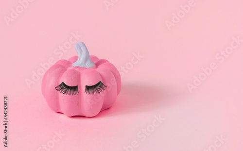 Halloween pink pumpkin with makeup, false eyelashes on the pink background, close-up