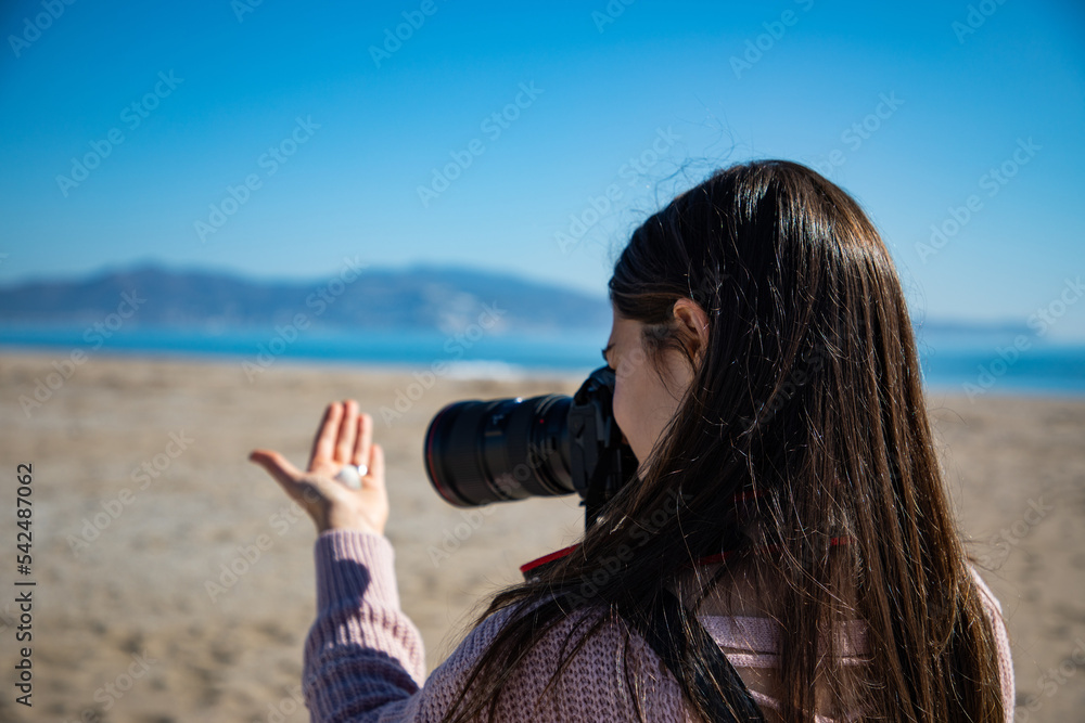 Beautiful woman taking a picture of a sea shell holding it with her hand