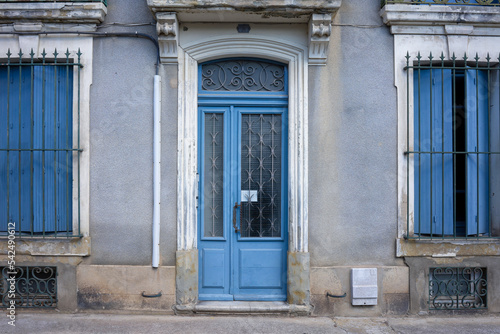 Front view of a facade of a traditional house in an old town of Carcassonne France. Blue shutters and wooden door. In front of it a sidewalk without people