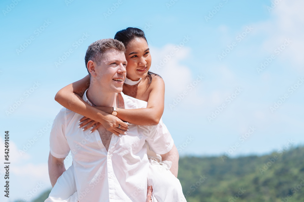 Young couple in love outdoor. Happy man giving piggyback ride to his woman and laughing at tropical beach. Girlfriend getting piggyback ride from boyfriend at sunrise in summer.