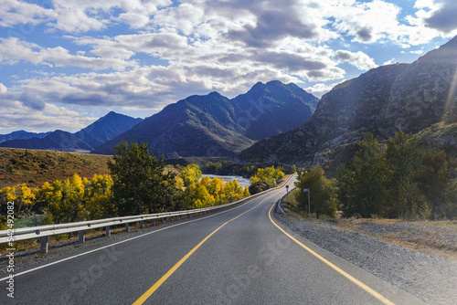 Fototapeta Naklejka Na Ścianę i Meble -  Serpentine asphalt road among high snow-capped mountain peaks, yellow desert, autumn green forest and blue sky. Car on the highway against the background of a mount landscape.