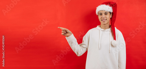 Portrait young man in a Christmas cap points with a finger, red background