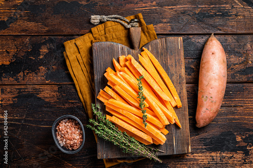 Sweet potatoes on a cutting board, fresh batata french fries ready for cooking. Wooden background. Top view photo