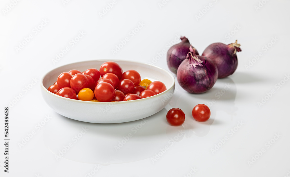 Small tomatoes in a white bowl with red onions Small tomatoes in a white bowl with red onions