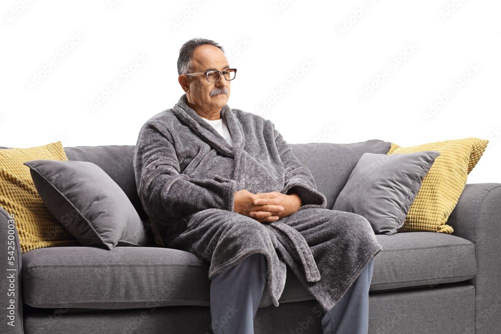 Pensive mature man wearing a bathrobe and sitting on a gray sofa