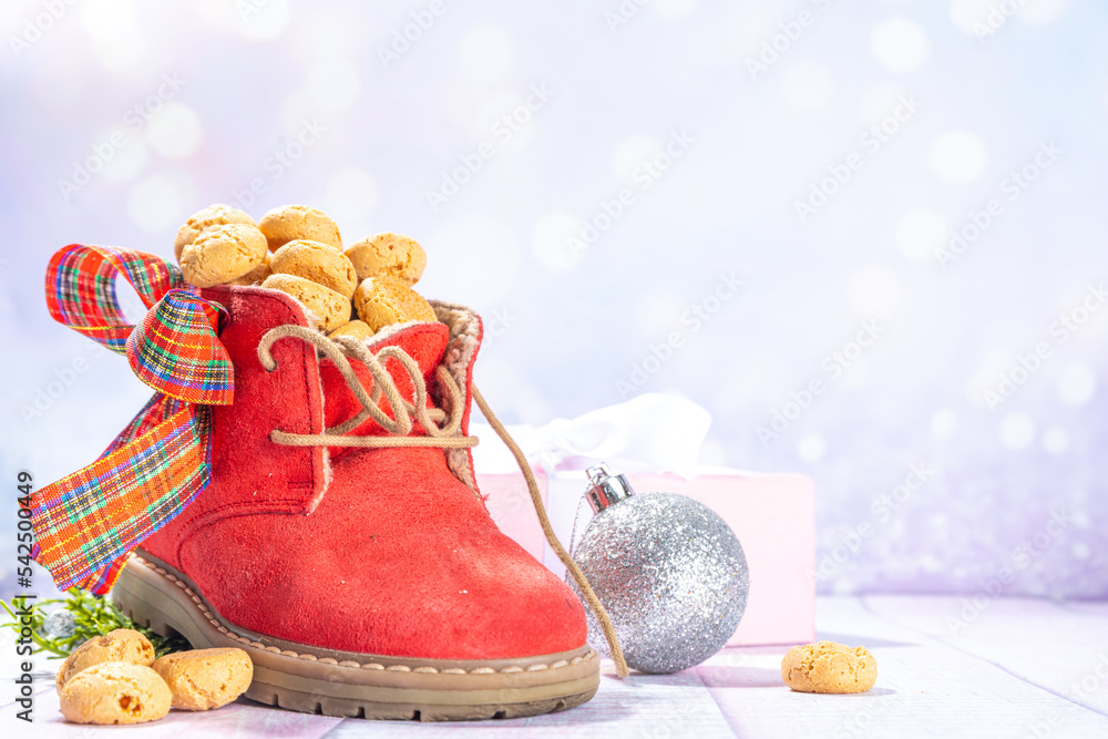 Sinterklaas, Saint Nicholas day background. Little kid red shoe with carrots and sweets, trooigoed, pepernoten, candy. Dutch Christmas holiday greeting card on snowy festive lights background copy spa Sinterklaas, Saint Nicholas day background. Little kid red shoe with carrots and sweets, trooigoed, pepernoten, candy. Dutch Christmas holiday greeting card on snowy festive lights background copy spa