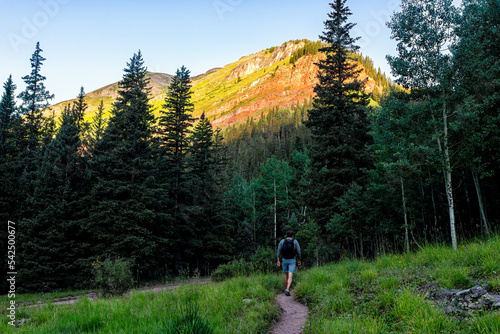 Man hiker walking on green alpine footpath trail to Ice lake near Silverton, Colorado in August early summer morning at sunrise with sunlight on peak photo