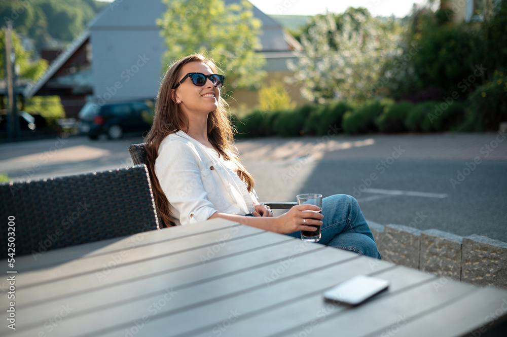 Relaxed woman with drink and mobile sitting on hotel terrace