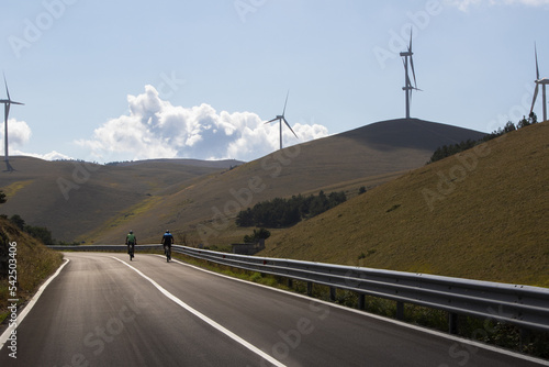 Men on bicycle in a day in the middle of nature among wind turbines in Italy. Sustainability in support of a green economy. Beautiful landscape