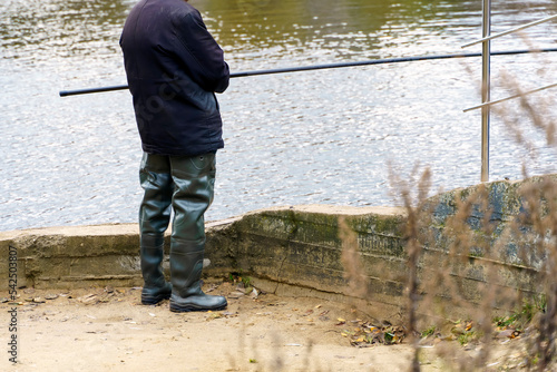 A fisherman in waist-high swamp boots stands on the bank of the river photo