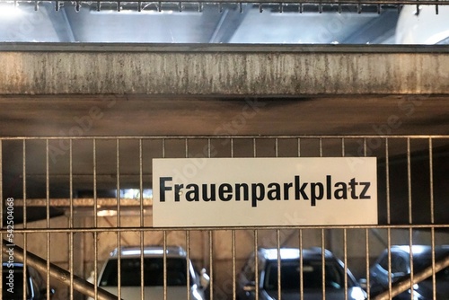 Innenausstattung von Parkhaus mit Gitterstäben, verwitterter weißgrauer Betonfassade, Autos und weißem Schild mit schwarzer Aufschrift - Frauenparkplatz  photo