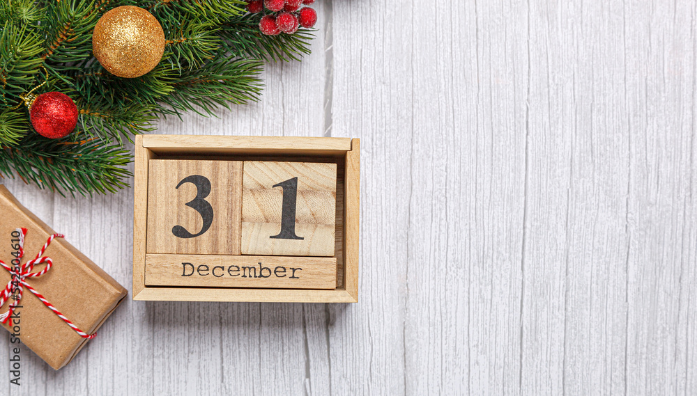 christmas tree branch with toys and gifts and wooden calendar december 31 on a wooden background