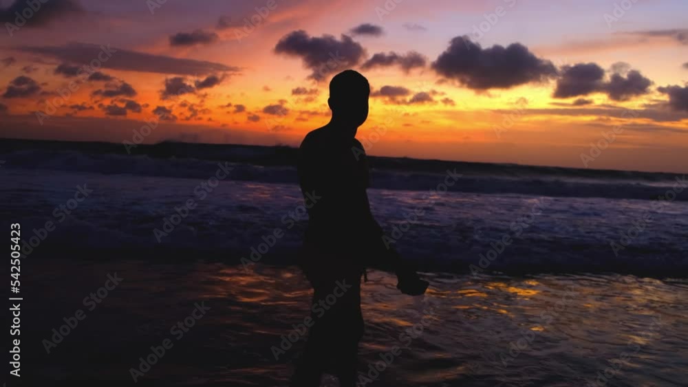 Silhouette of man walking on the beach at sunset, recreating at tropical island on vacations, relaxed lifestyle. Man enjoys a beautiful fiery sunset during an evening walk along the ocean. Silhouette of man walking on the beach at sunset, recreating at tropical island on vacations, relaxed lifestyle. Man enjoys a beautiful fiery sunset during an evening walk along the ocean.