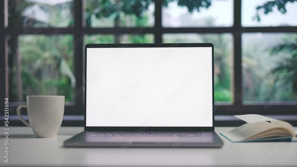 White desk with laptop, notepad and cup of steaming coffee, computer with blank screen of copy space before window and trees view White desk with laptop, notepad and cup of steaming coffee, computer with blank screen of copy space before window and trees view