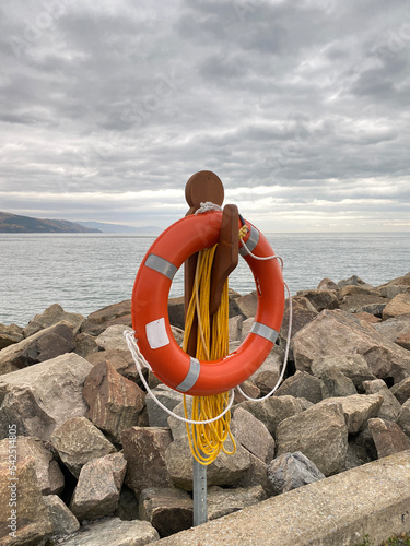 Bouée de sauvetage orange sur le bord d'une jetée. Anneau de sécurité pour des sauvetage en mer. Bouée de sécurité sur un quai. Paysage nuageux d'une plage. Concept de noyade et de vie en danger.