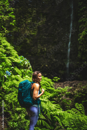 Sporty woman marvels at nature at an impressive waterfall in the jungle with beautiful flowers and ferns. Levada of Caldeirão Verde, Madeira Island, Portugal, Europe. © Michael