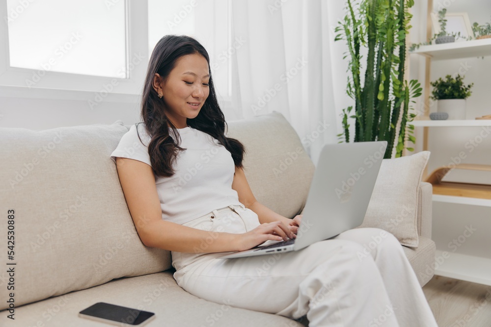 Young Asian woman looking at laptop screen on her lap sitting on couch at home lifestyle work as a freelancer Young Asian woman looking at laptop screen on her lap sitting on couch at home lifestyle work as a freelancer
