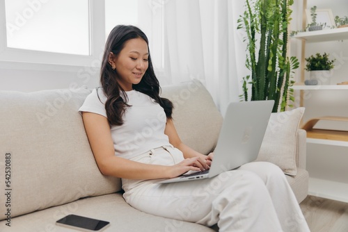Young Asian woman looking at laptop screen on her lap sitting on couch at home lifestyle work as a freelancer