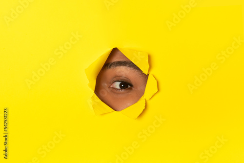 Curious African Woman Peeking Through Hole In Torn Yellow Paper © Prostock-studio