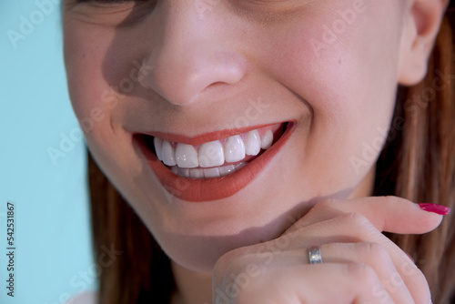 Beautiful smile of young caucasian brunette woman with healthy white teeth against blue background. Close-up view. Selective focus. Dental care theme.