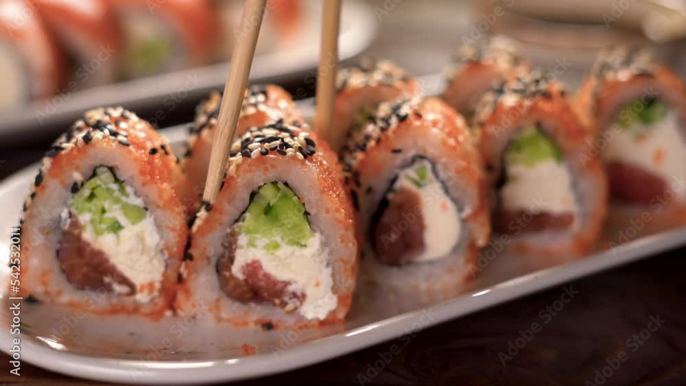 Eating Sushi with chopsticks. sushi roll japanese food in restaurant. Sushi with salmon, vegetables, caviar, close up. Japan restaurant menu Eating Sushi with chopsticks. sushi roll japanese food in restaurant. Sushi with salmon, vegetables, caviar, close up. Japan restaurant menu