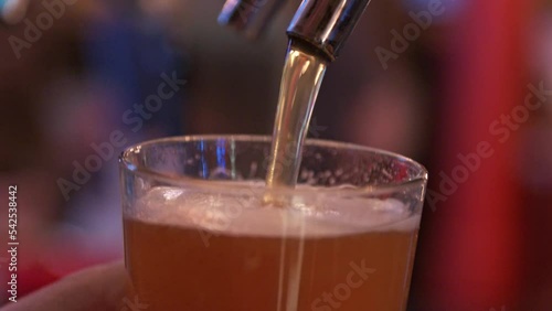 draft beer being poured into a clear glass using a metal draft keg in a dark and busy bar 