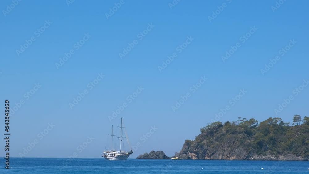One sailboat in turquoise lagoon. A view of sailboat floating in the turquoise lagoon by the green hills. A concept of summer traveling and sea touristic life. One sailboat in turquoise lagoon. A view of sailboat floating in the turquoise lagoon by the green hills. A concept of summer traveling and sea touristic life.