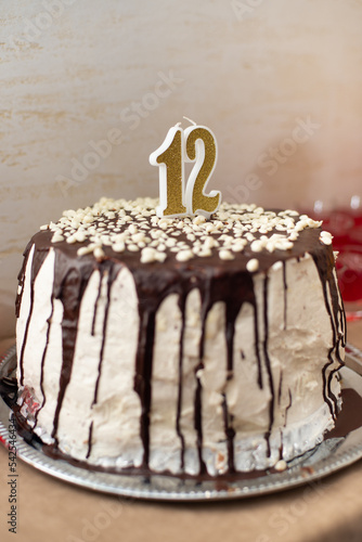 Homemade round sponge cake or chiffon cake buisquit with white cream and chocolate chocolate smudges. 12th birthday pie with holiday candles. Vertical photo, soft focus, blurry photo