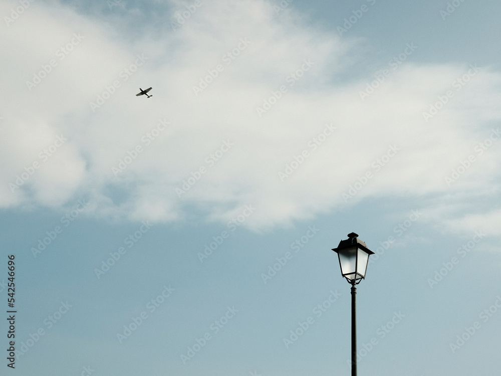 Black lantern under blue sky with flying plane