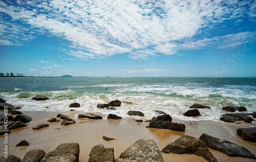 Looking north from Alexandra Headland beach, a coastal part of Maroochydore,Sunshine Coast, Queensland, Australia. Rocky foreshore with waves breaking and cloudy blue sky.