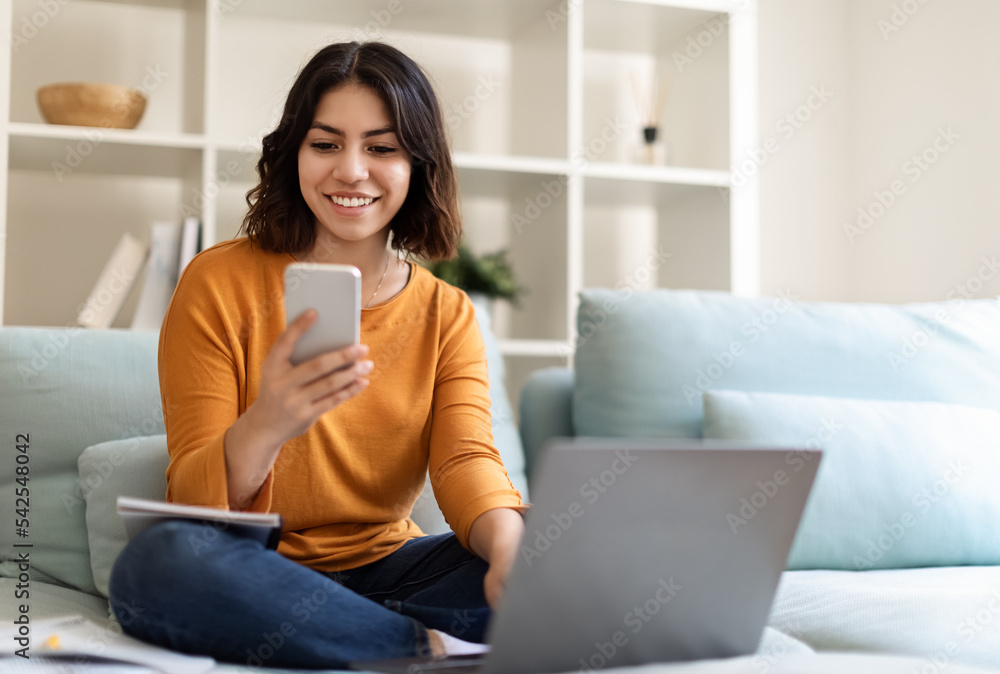 Young Middle Eastern Female Relaxing On Couch With Smartphone And Laptop Young Middle Eastern Female Relaxing On Couch With Smartphone And Laptop