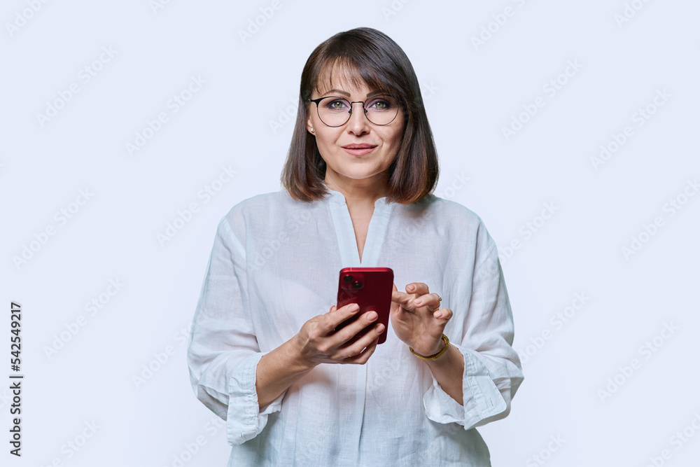 Portrait of middle aged woman with phone looking at camera on white background Portrait of middle aged woman with phone looking at camera on white background