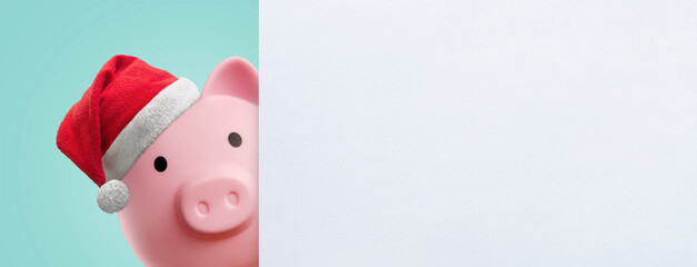 pink piggy bank with christmas hat behind a white sign - copy space