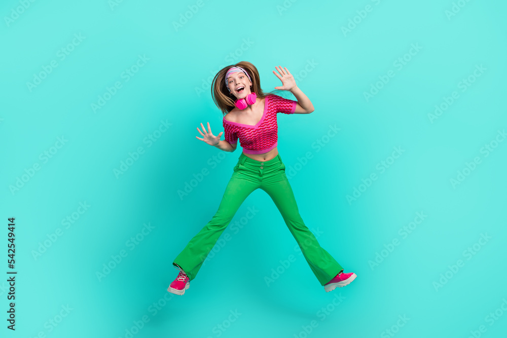 Full length photo of pretty cute school girl dressed pink crop top flared pants jumping high rising hands arms isolated teal color background