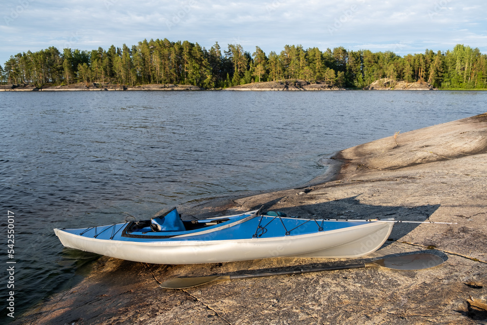 Blue kayak on the stone of a large lake. An oar lies on a rocky shore. Spinning for catching fish on the bow of the boat Blue kayak on the stone of a large lake. An oar lies on a rocky shore. Spinning for catching fish on the bow of the boat