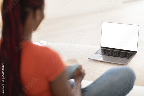 Black Woman Using Laptop With White Screen And Drinking Coffee At Home