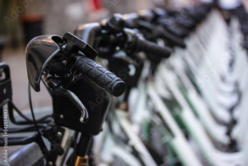 Lots of white bicycles stand in a row in bicycle parking lot. Renting and sharing bikes. Eco-friendly transportation for sports, travel in a city. Green transport rent. Handlebars, wheels, bike frames