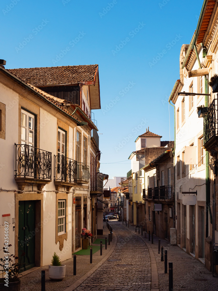 View of empty narrow street in Portuguese city of Vila Real with townhouses decorated with forged balconies on sunny spring day .