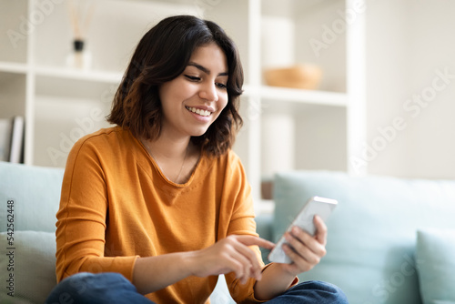 Happy Young Arab Female Messaging On Smartphone While Relaxing At Home