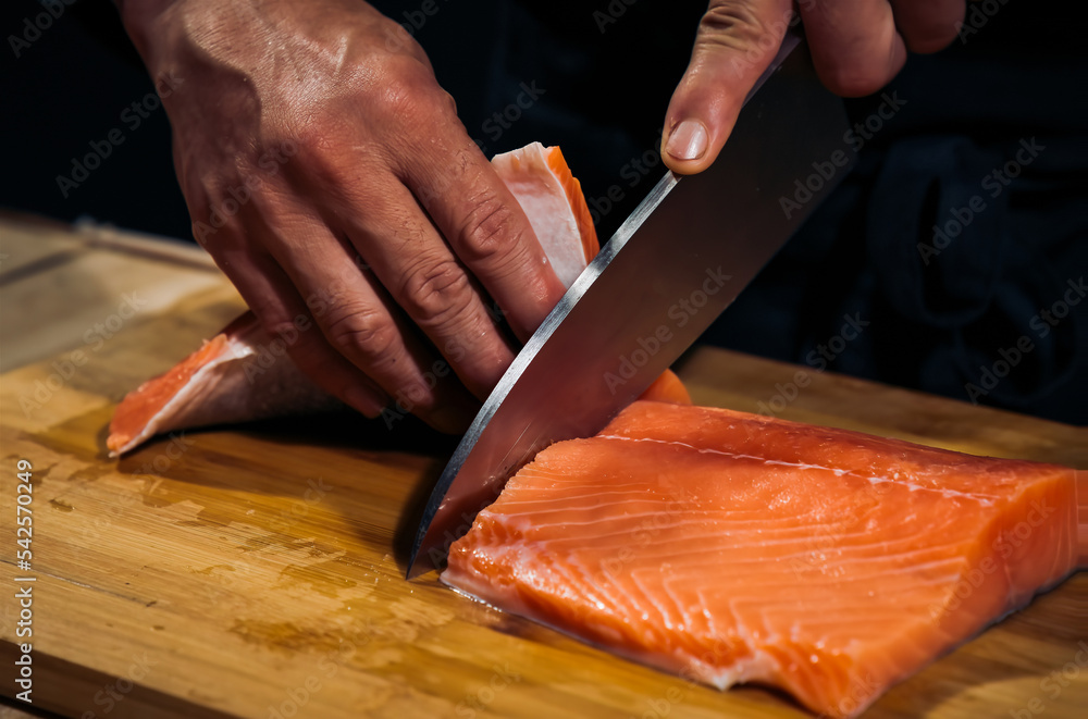 Close up of Chef cook hands chopping salmon fish for traditional Asian cuisine with Japanese knife. Professional Sushi chef cutting seafood japanese chefs are making salmon fish sashimi. dark tone