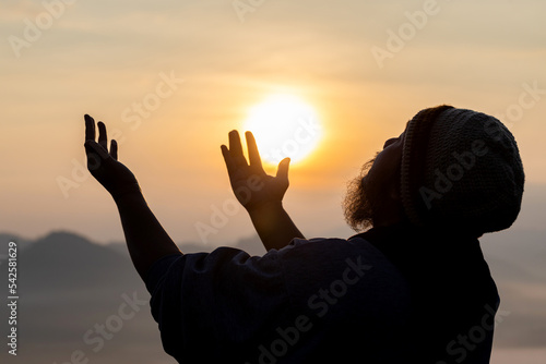 Silhouette Portrait of young adult male with beard praying for thank god golden sunset sky background.