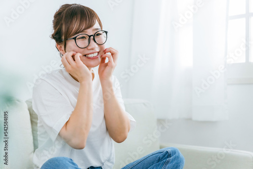 ソファに座りながら照れて爆笑するメガネをかけたアジア人女性 