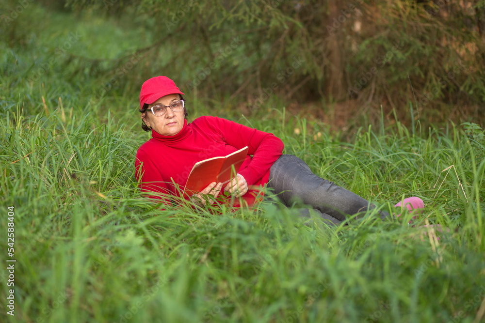 beautiful mature woman lies on a green meadow in the forest and reads a book beautiful mature woman lies on a green meadow in the forest and reads a book