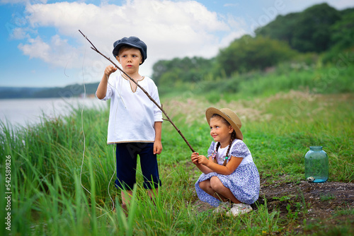 Two kids are fishing by the water. A boy and a girl with a fishing rod catch everything from the lake.