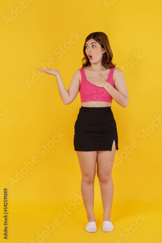 Portrait of Surprised young woman presenting or showing open hand palm with copy space for product over isolated yellow background